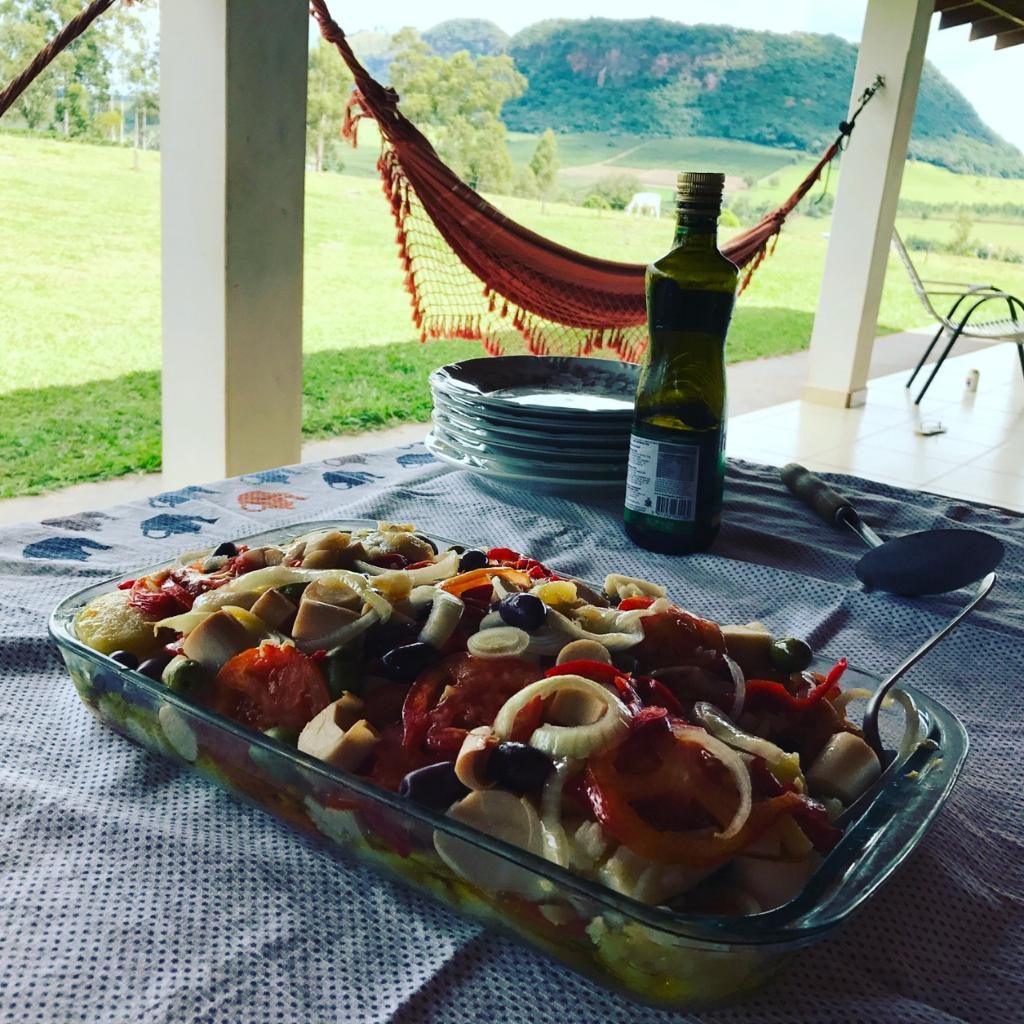 Travessa de comida na mesa da varanda, com rede e vista do morro